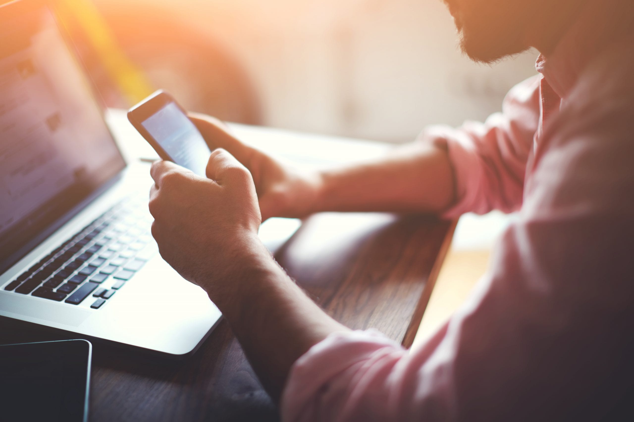 Man in front of a laptop holding a mobile phone representing PPC advertising.