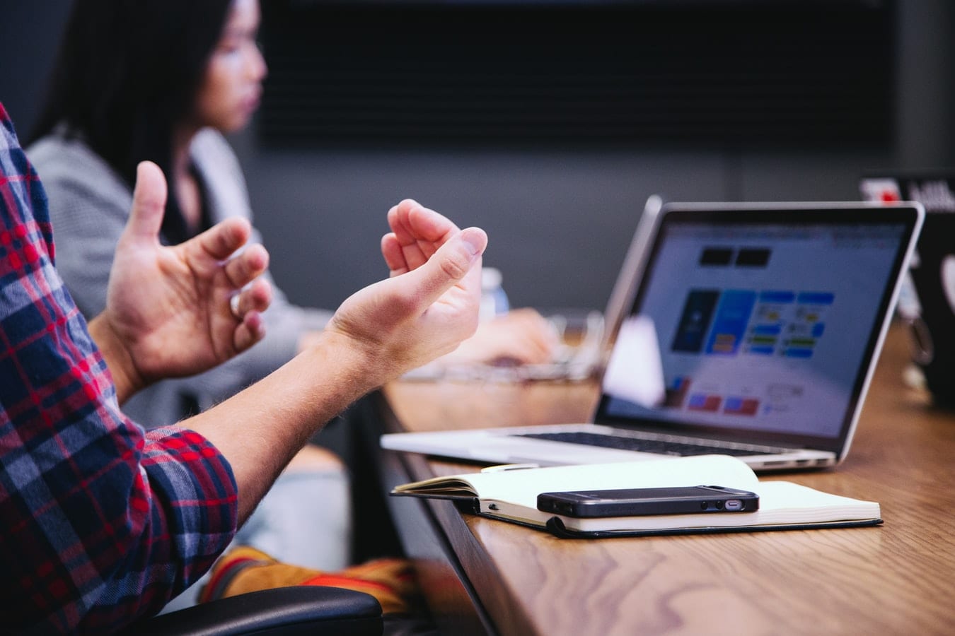 Person gesturing with hands in front of laptop while at a meeting.