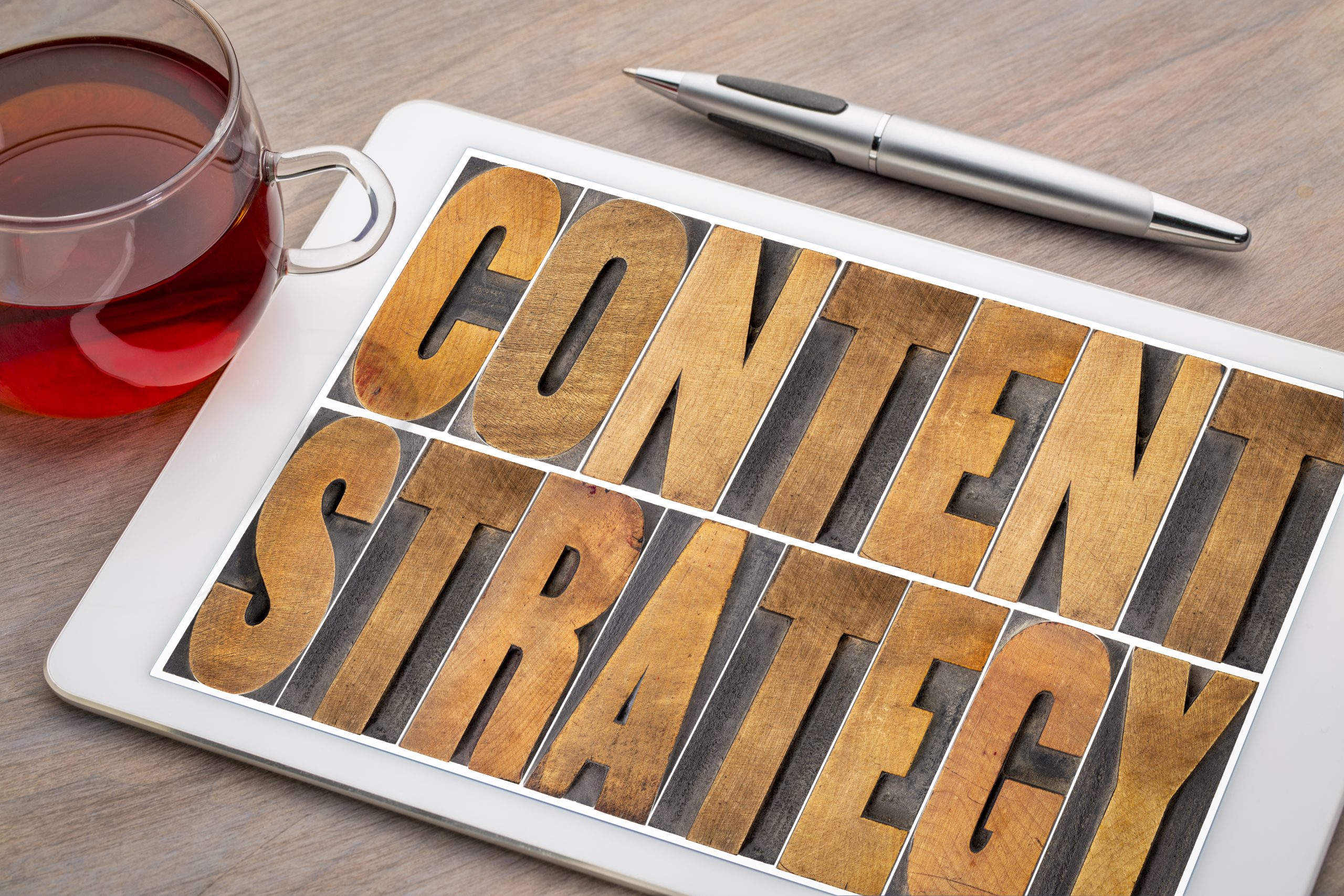 content strategy - word abstract in letterpress wood type printing blocks on a digital tablet with cup of tea