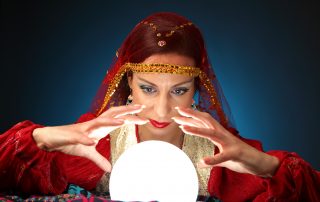 Woman dressed in fortune-tellers costume peering into a lighted crystal ball.