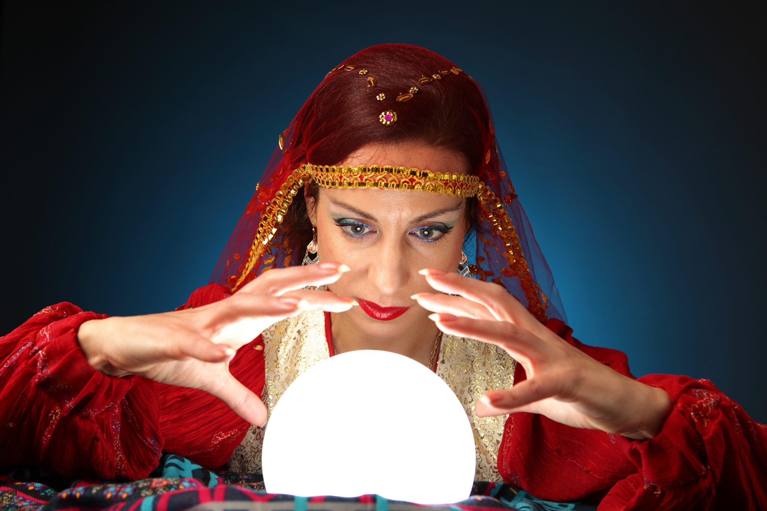 Woman dressed in fortune-tellers costume peering into a lighted crystal ball.