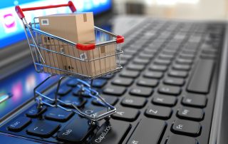 Tiny shopping cart with cardboard boxes on top of laptop keyboard signifying Ecommerce