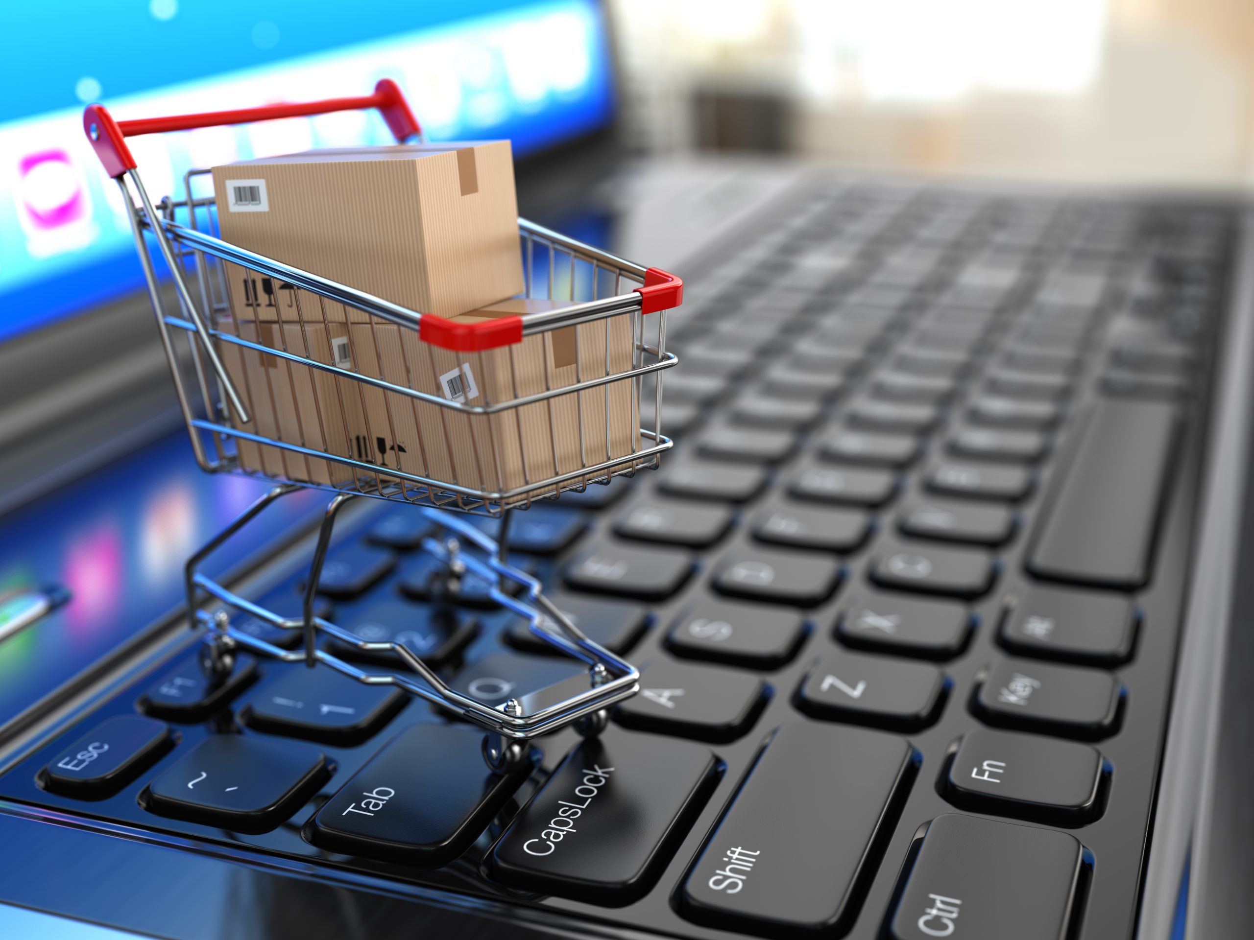 Tiny shopping cart with cardboard boxes on top of laptop keyboard signifying Ecommerce