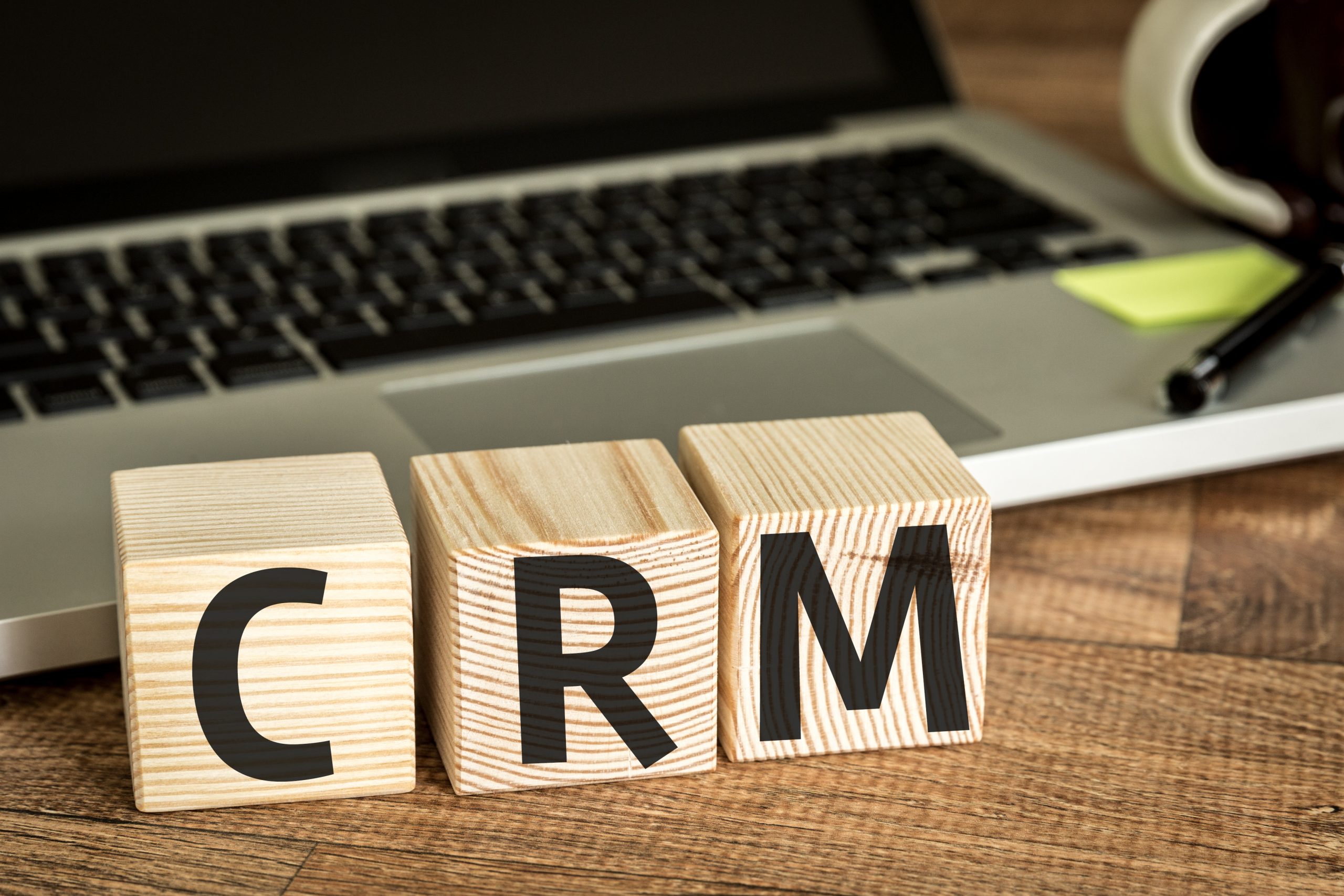 Laptop keyboard behind three wooden blocks that have the letters "CRM". 