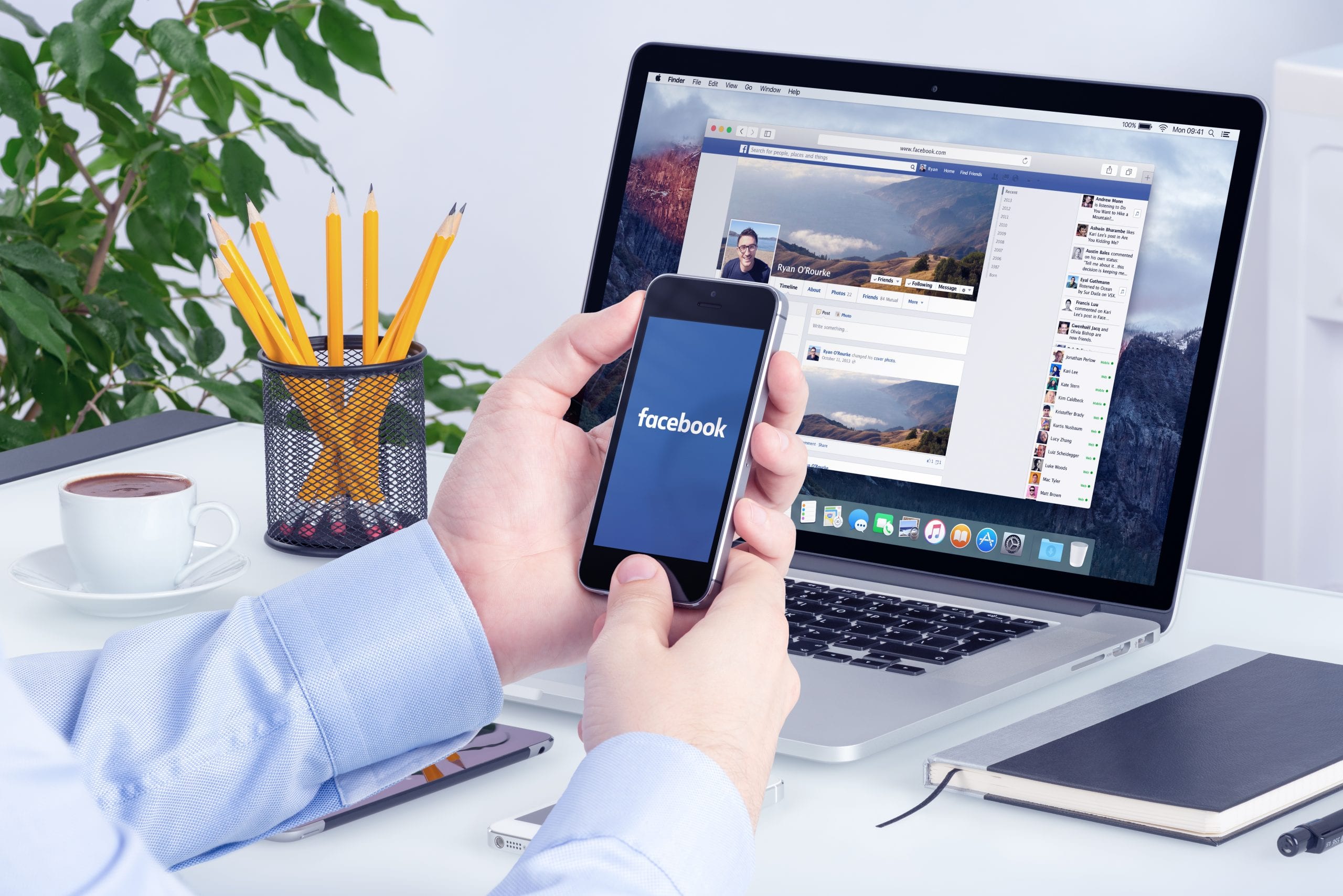 Small business owner at a desk using Facebook on his mobile device and laptop which represents Facebook retargeting.