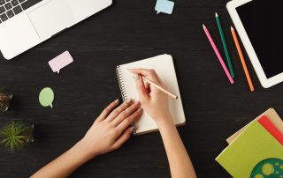 Woman's hands writing on a notebook at her desk symbolizes content creation.