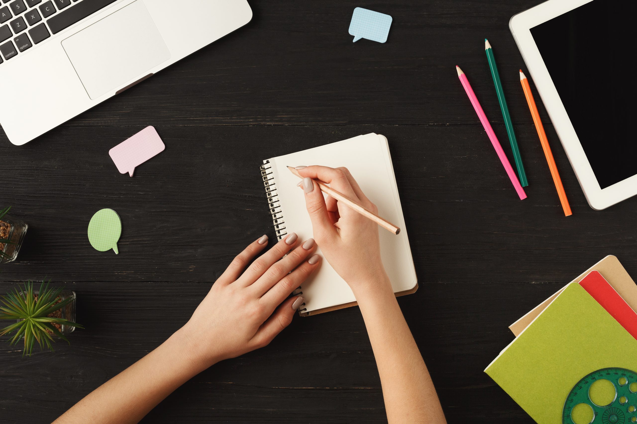 Woman's hands writing on a notebook at her desk symbolizes content creation.