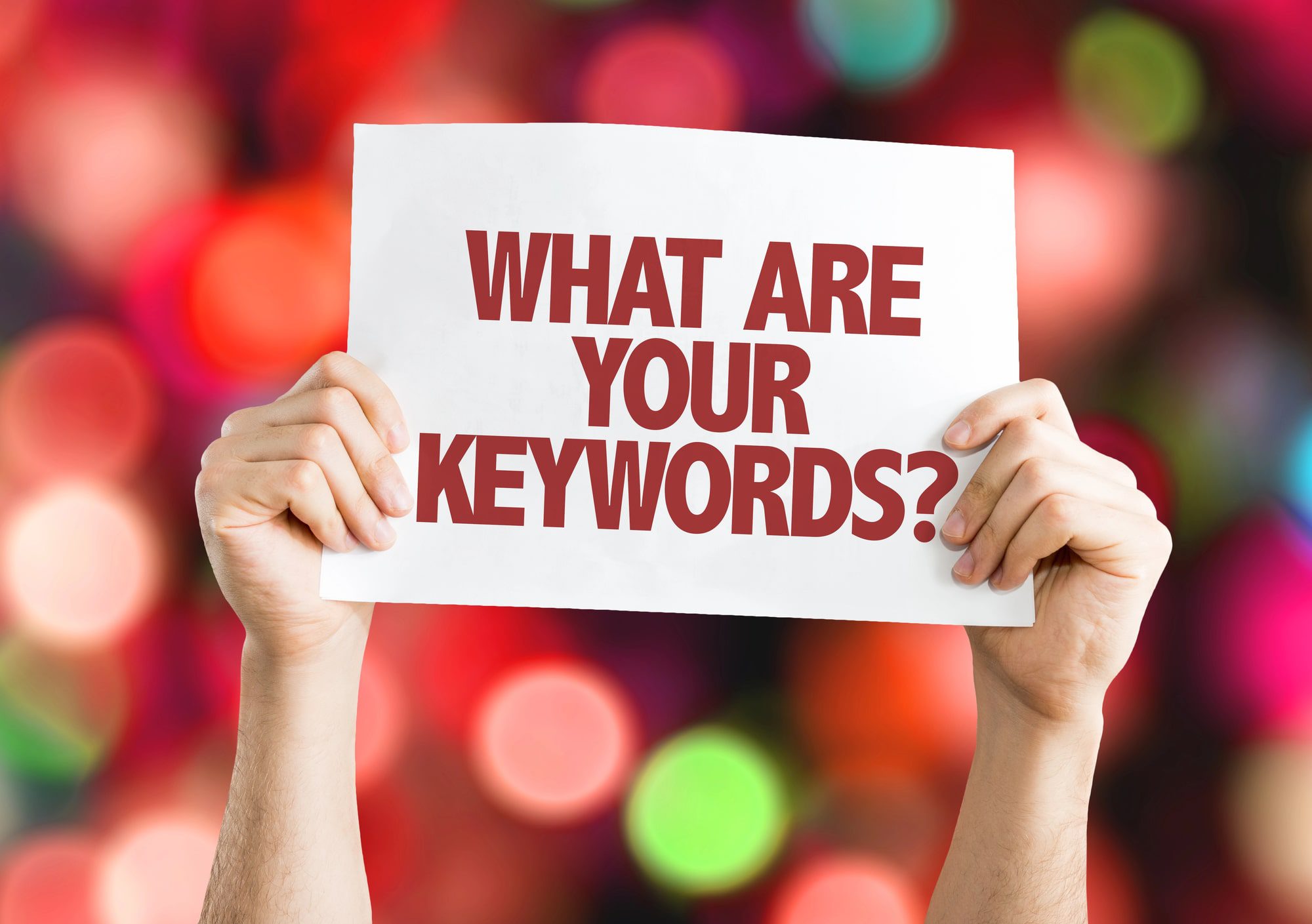 person holding a paper sign that reads "WHAT ARE YOUR KEYWORDS?"